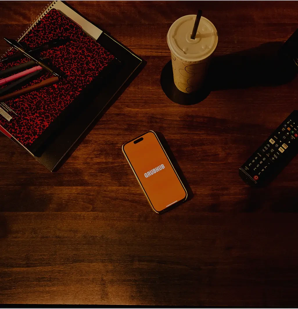 A smartphone atop a wooden desk displaying the Grubhub logo